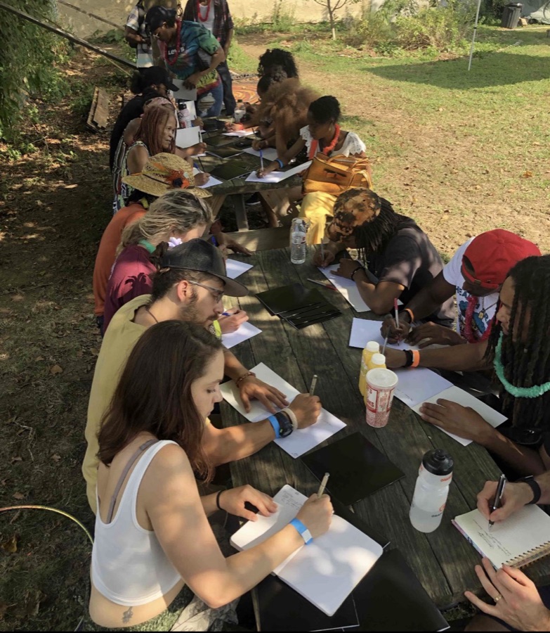 A long outdoor table, everyone writing